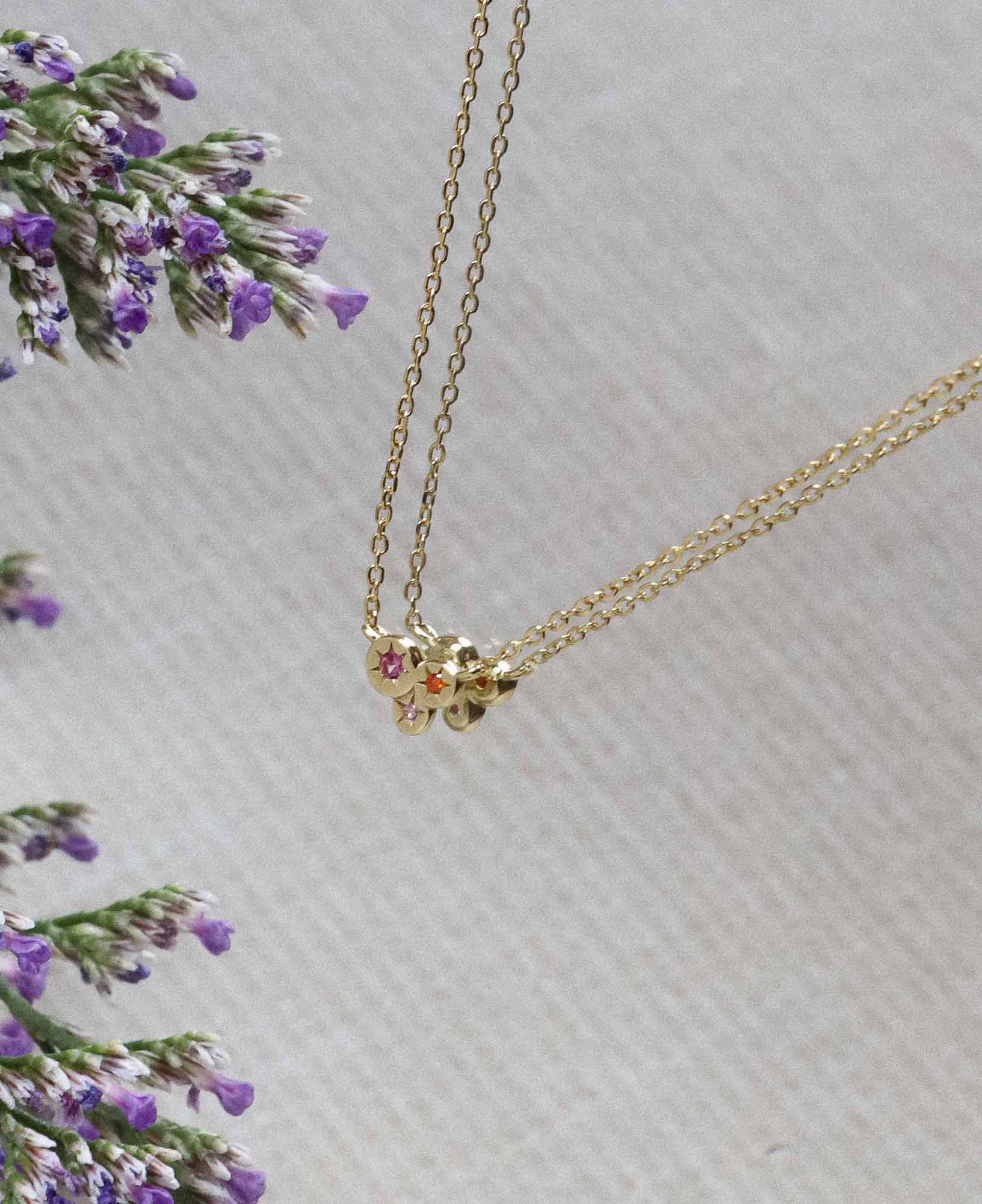 flat lay product picture of the Lisette Star Burst CZ Pendant Necklace placed on a mirror near some purple flowers.