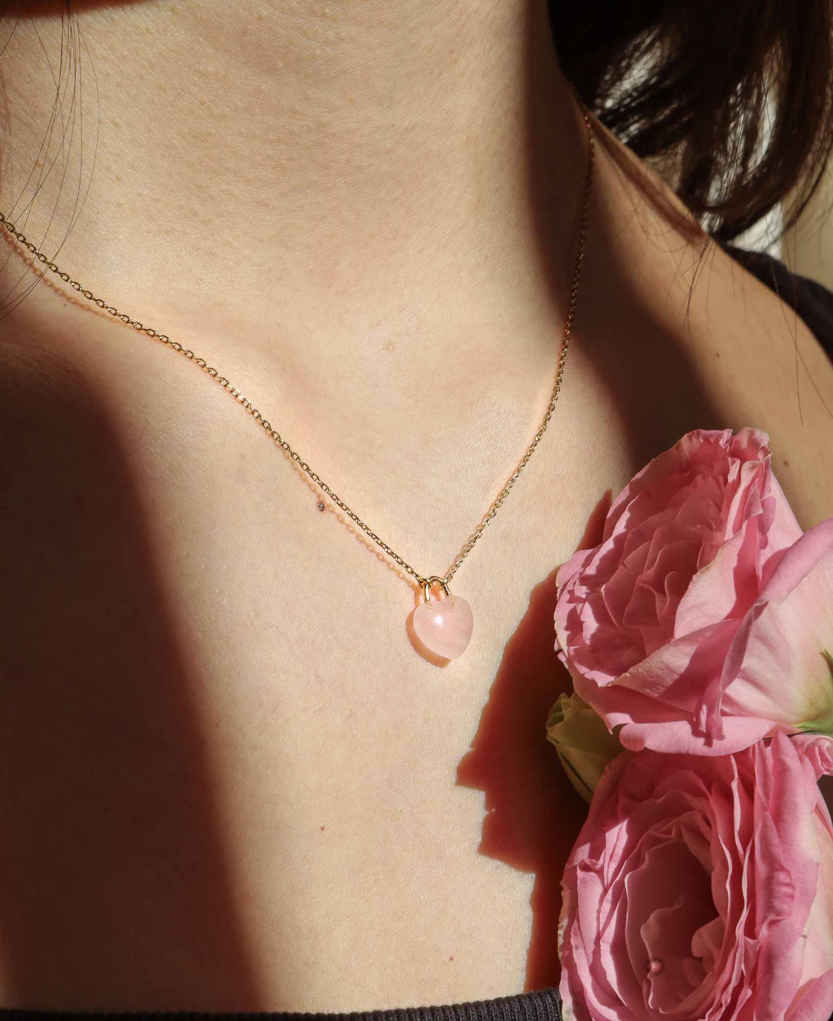 the Desiree Eternal Heart Rose Quartz Pendant Necklace featured on a model, decorated with some seasonal pink flowers.