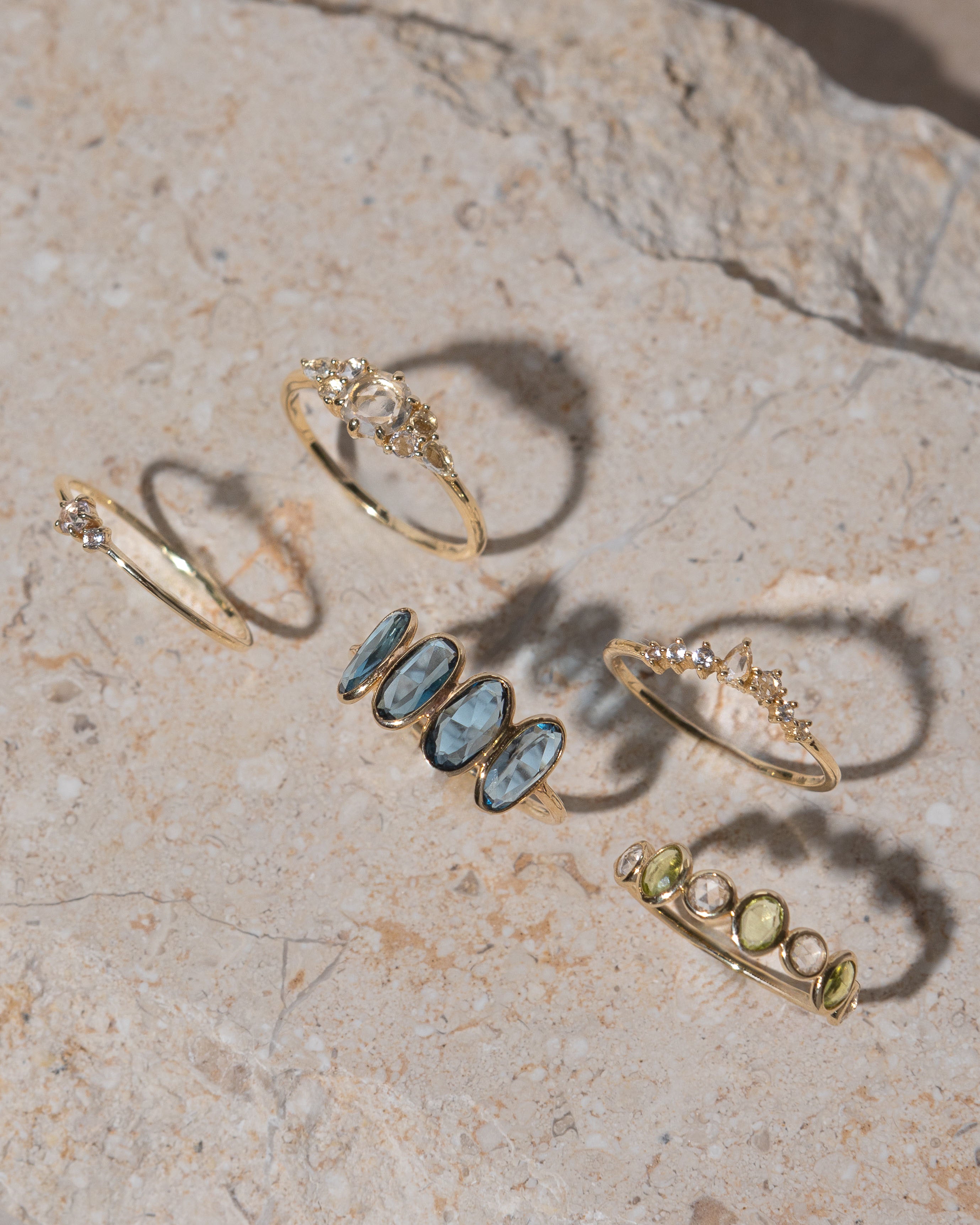 lifestyle product shot of genevieve half eternity solid gold ring, marjorie blue topaz solid gold ring, josephine white sapphire cluster solid gold ring, ophelia white sapphire solid gold ring and cleo white sapphire solid gold ring