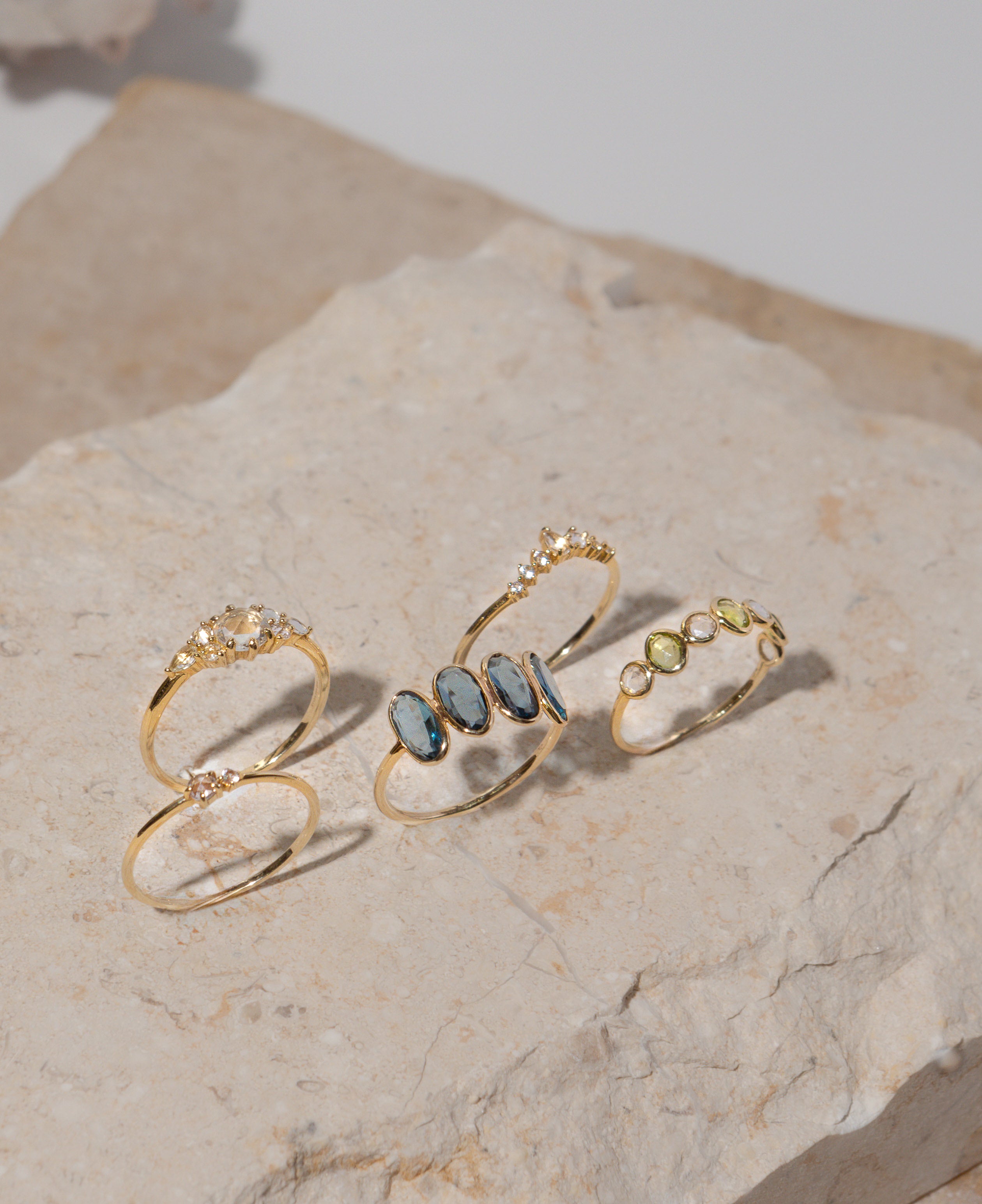lifestyle product shot of cleo white sapphire solid gold ring, genevieve half eternity solid gold ring, marjorie blue topaz solid gold ring, josephine white sapphire cluster solid gold ring, ophelia white sapphire solid gold ring