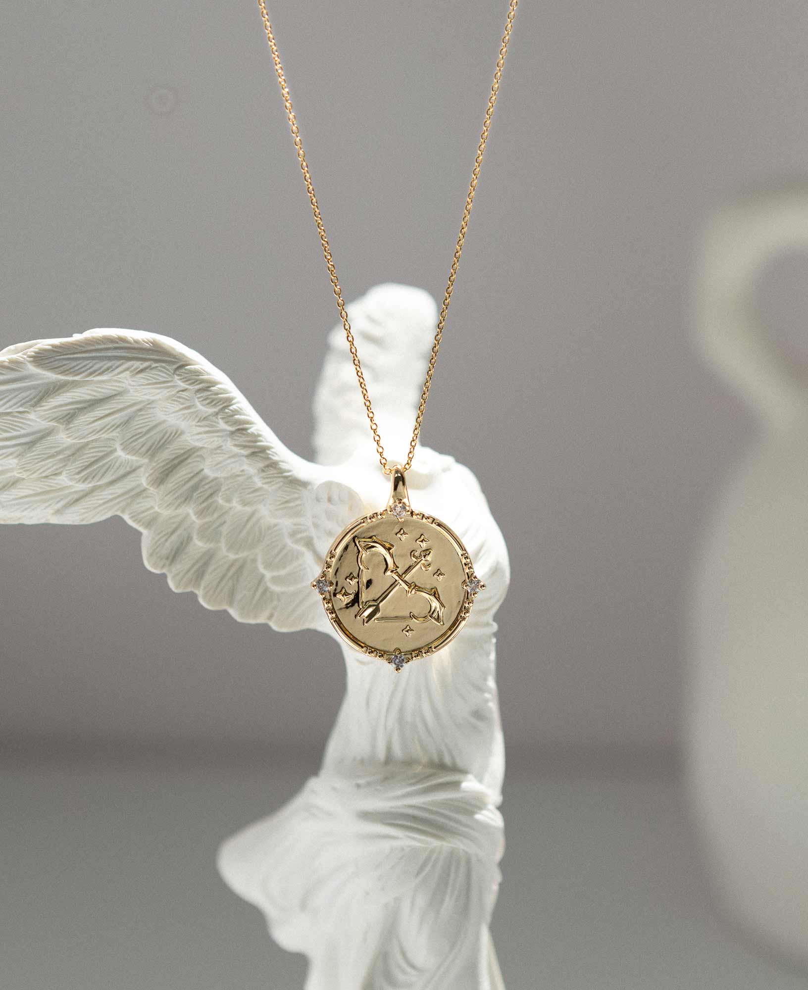 artistic close-up lifestyle product picture of Sagittarius Horoscope Gold Pendant Necklace dangled on a white marble greek goddess statue.