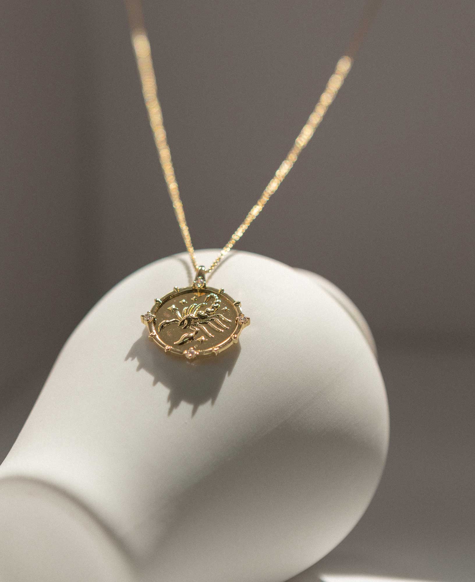 artistic close-up image exhibiting the Scorpio Horoscope Gold Pendant Necklace on a white ceramic vase.