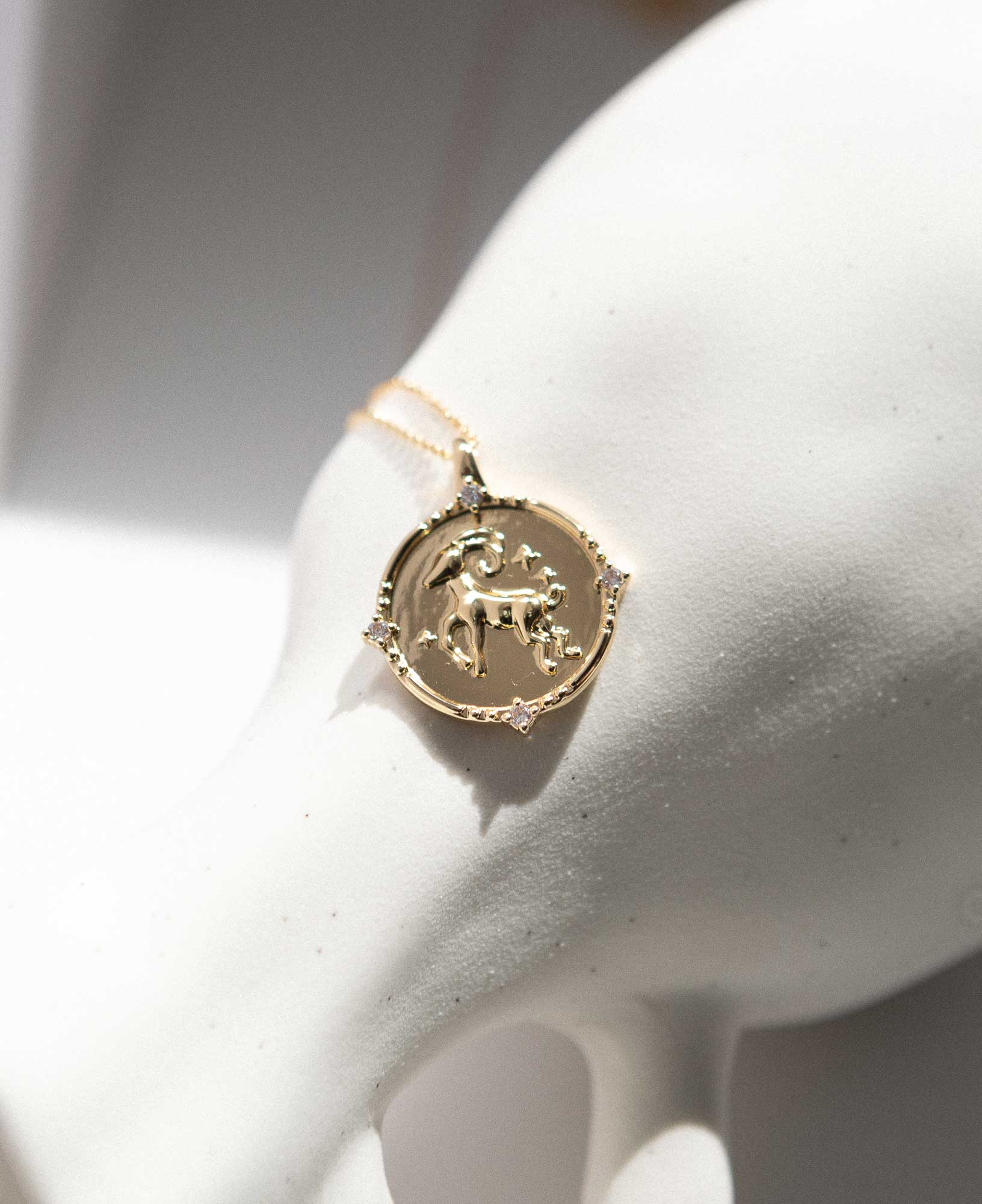 Artistic close-up shot of Aries Horoscope Gold Pendant Necklace placed delicately on a white ceramic vase.