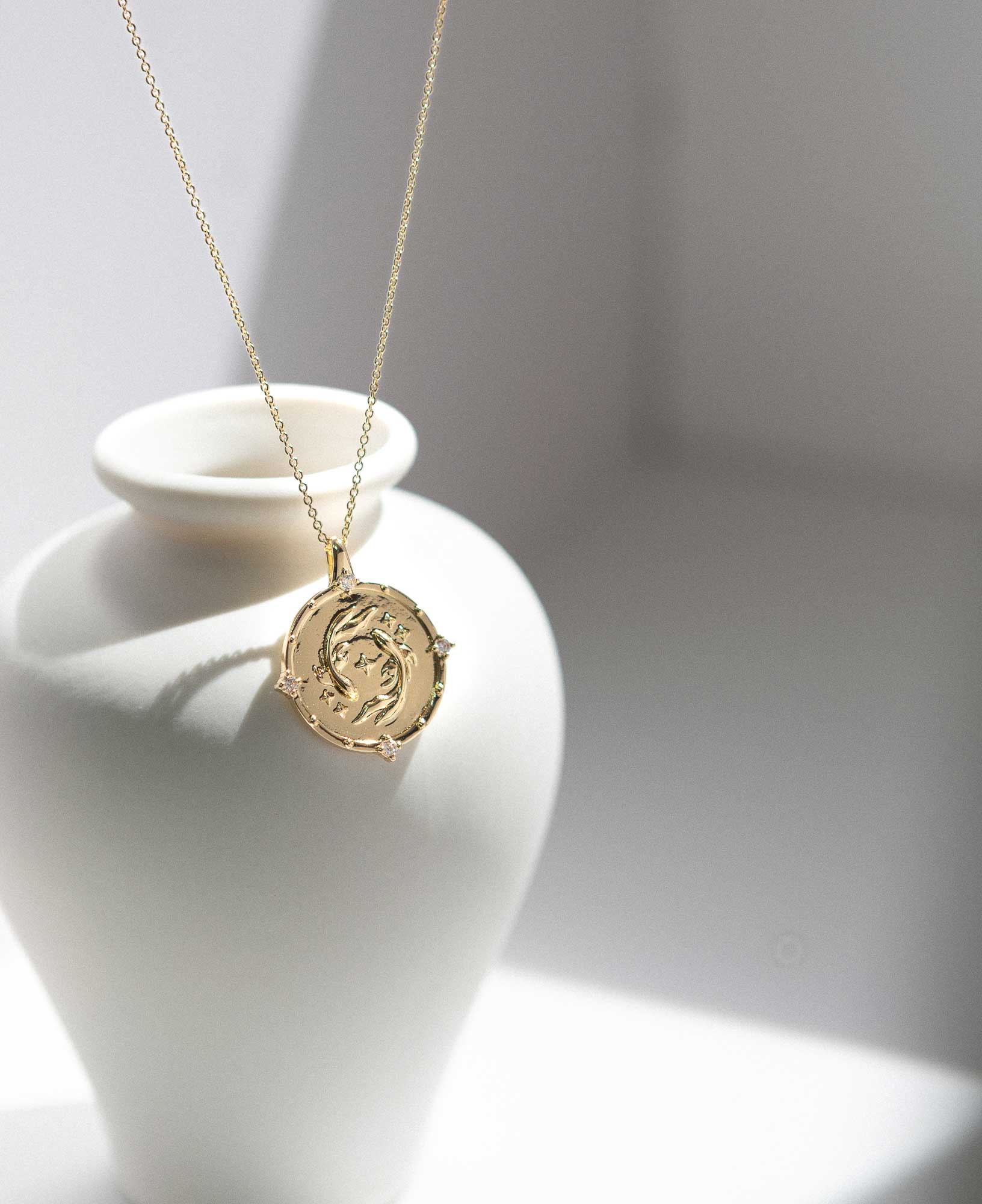 artistic close-up lifestyle image displaying Pisces Horoscope Gold Pendant Necklace on a white ceramic vase.