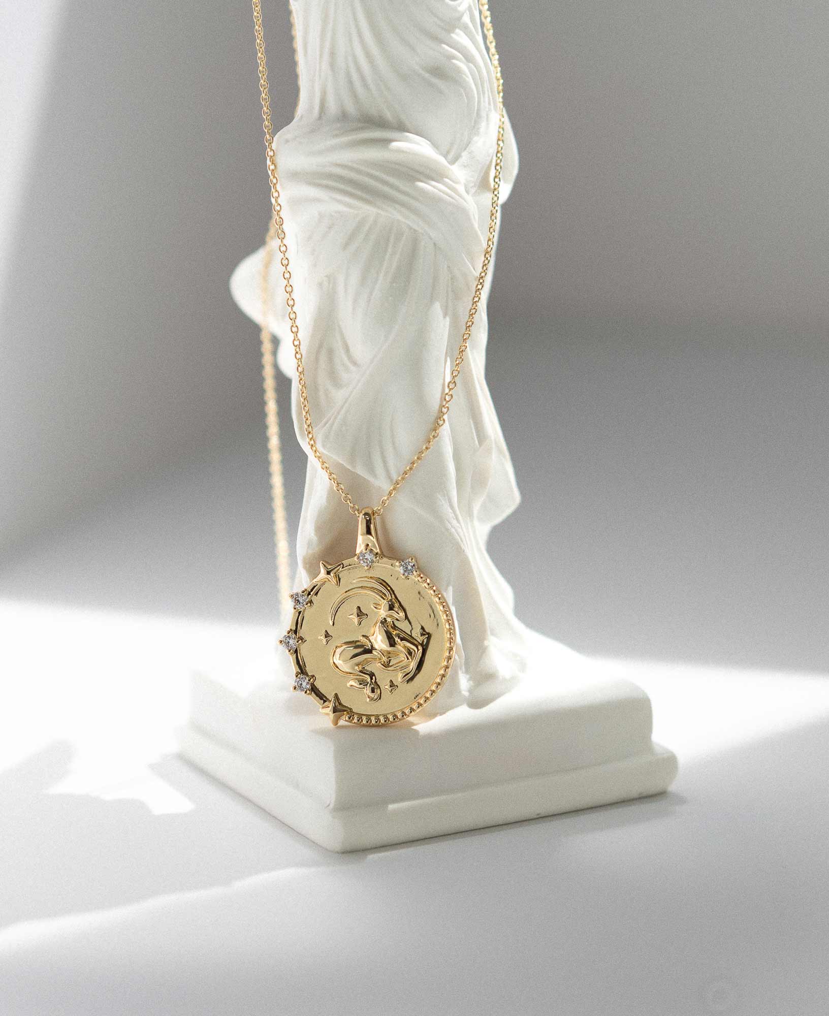 artistic close-up lifestyle product image of Capricorn Horoscope Gold Pendant Necklace on white marble greek goddess statue.