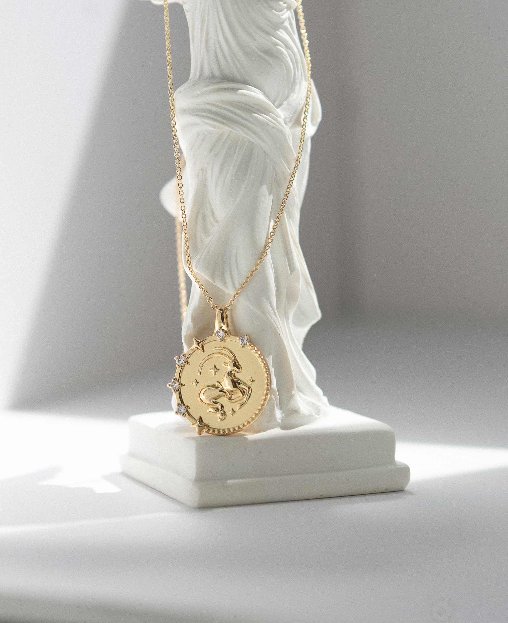 artistic close-up lifestyle product image of Capricorn Horoscope Gold Pendant Necklace on white marble greek goddess statue.