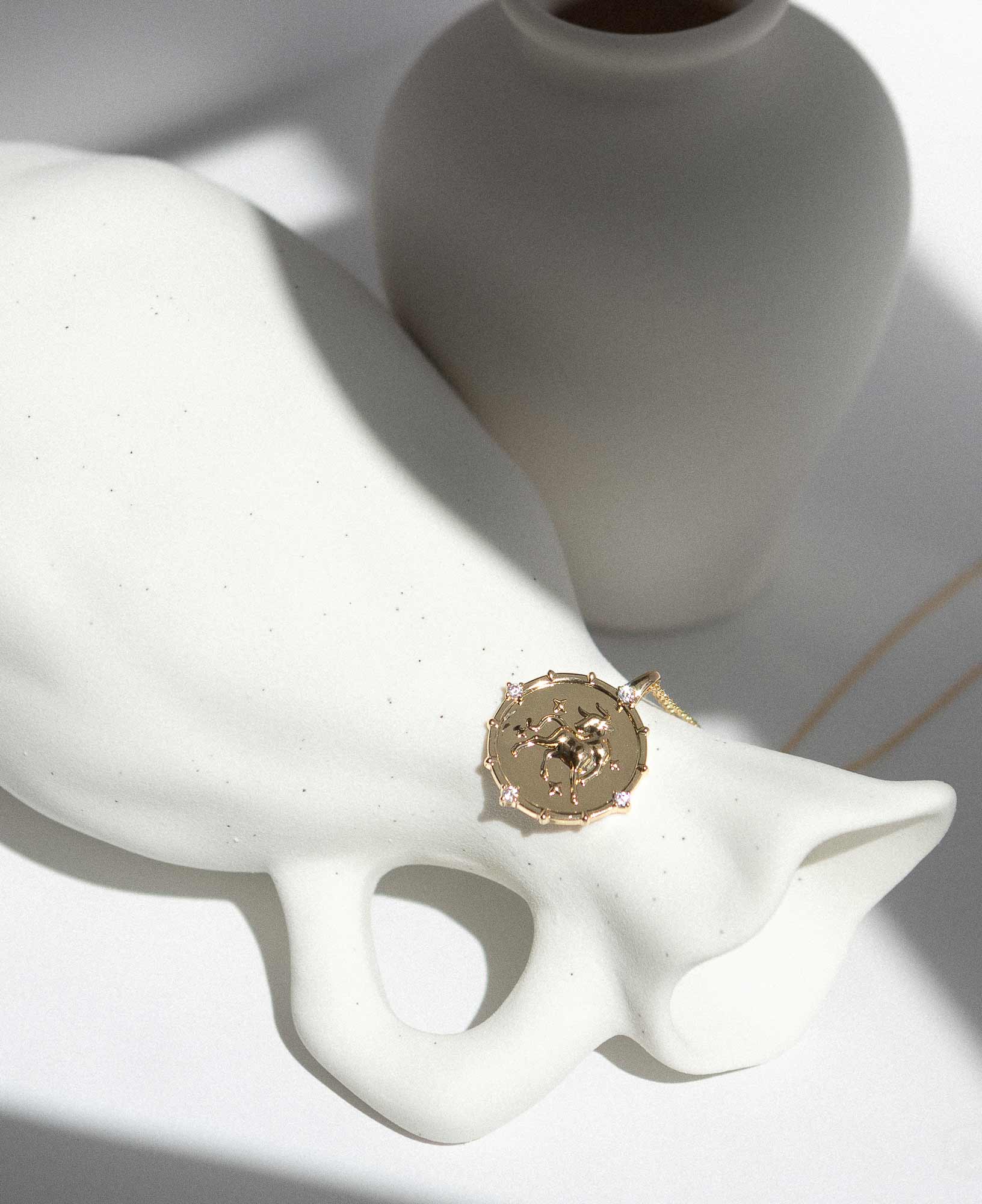 Artistic lifetyle picture of Taurus Horoscope Gold Pendant Necklace on white ceramic vase.