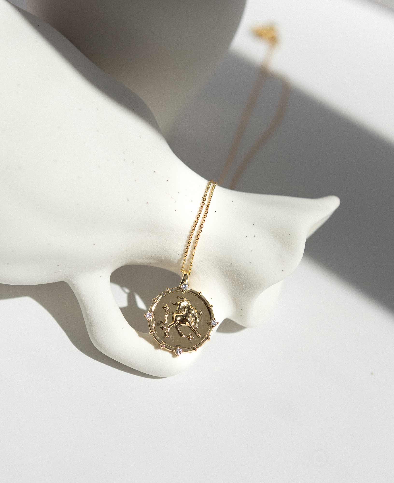 Artistic lifetyle picture of Taurus Horoscope Gold Pendant Necklace on white ceramic vase.