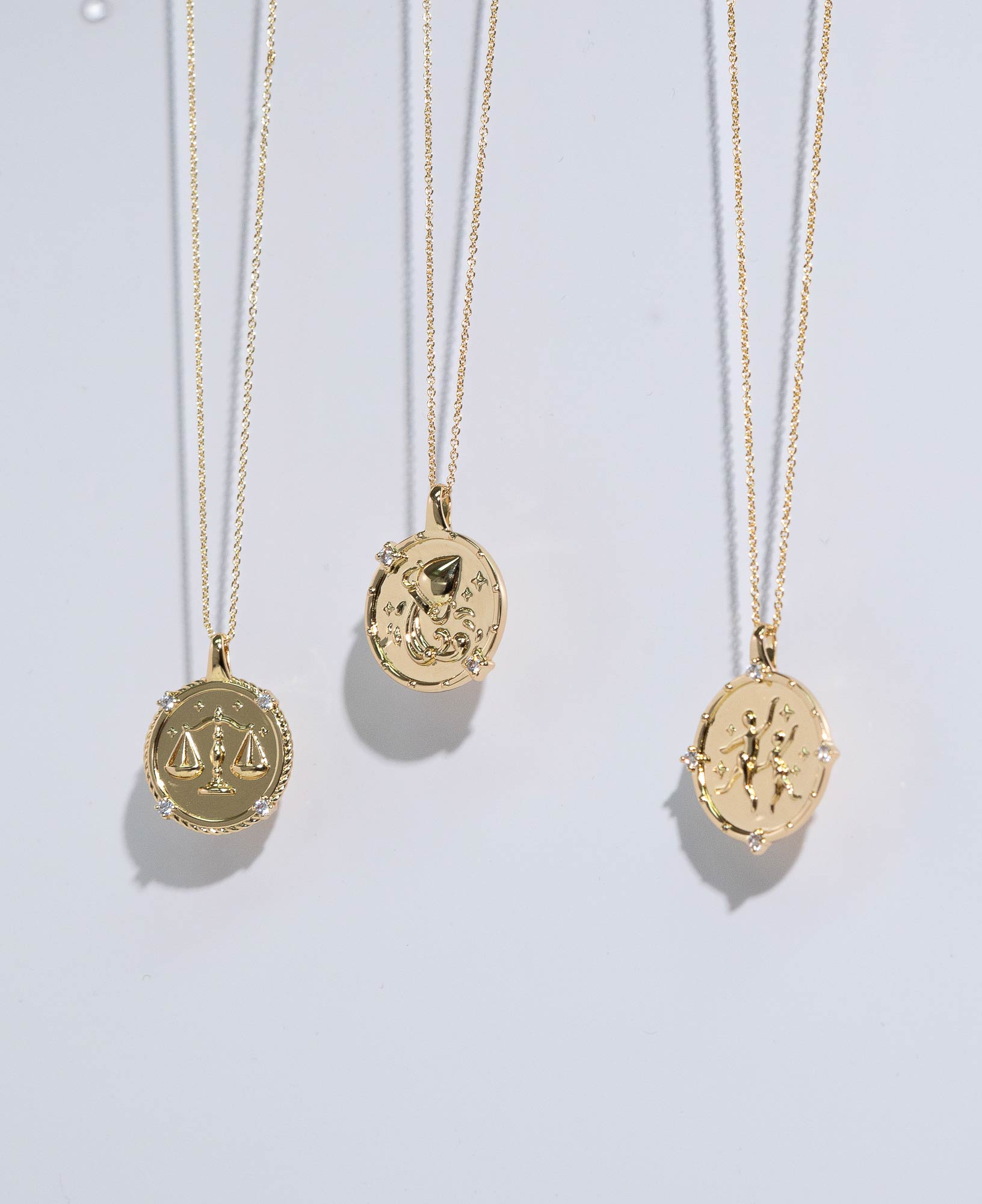 artistic lifestyle product image showcasing Libra, Aquarius and Gemini Horoscope Gold Pendant Necklaces in front of a white background.