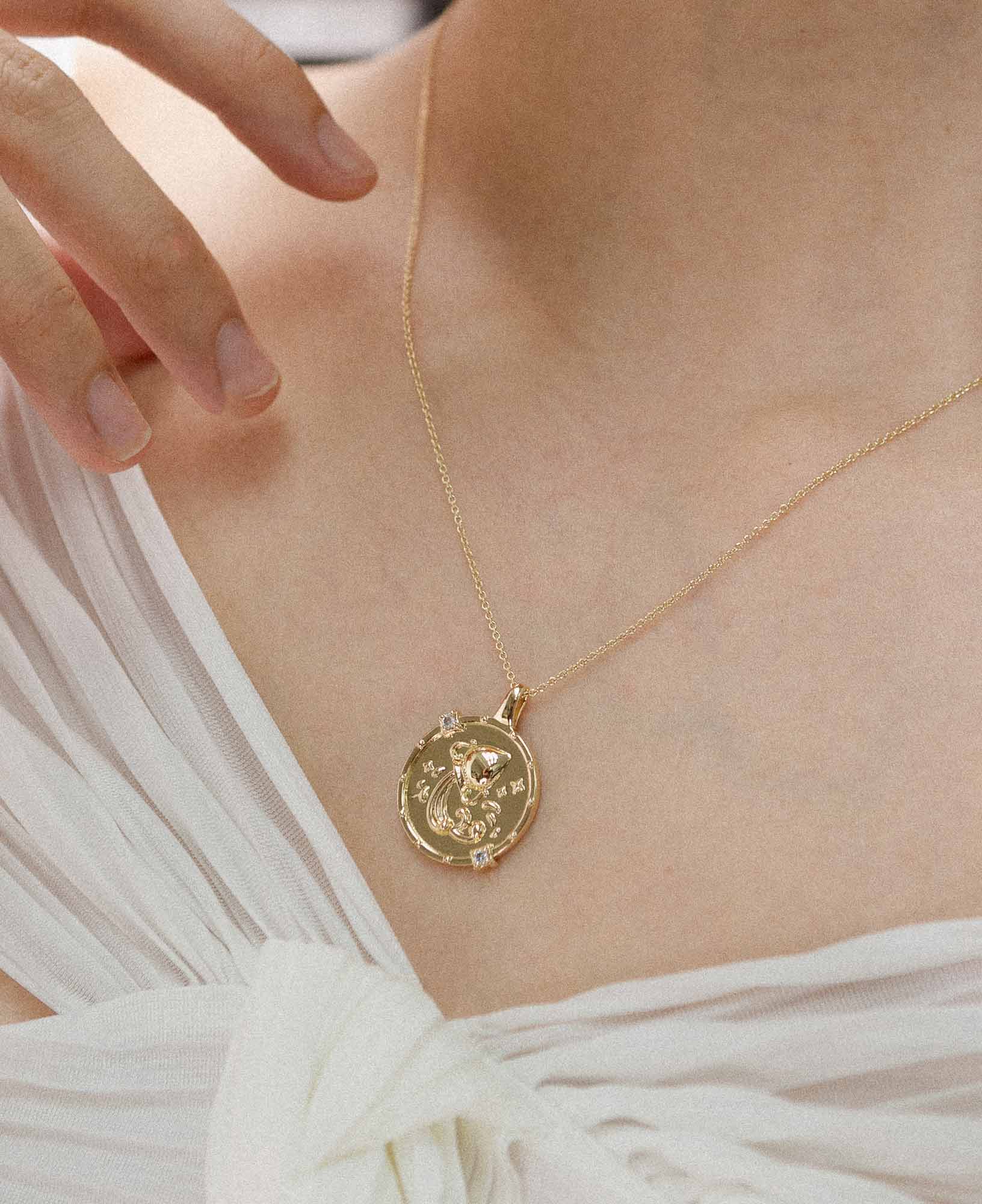 model styling the aquarius horoscope gold pendant necklace with a white off-shoulder chiffon top.