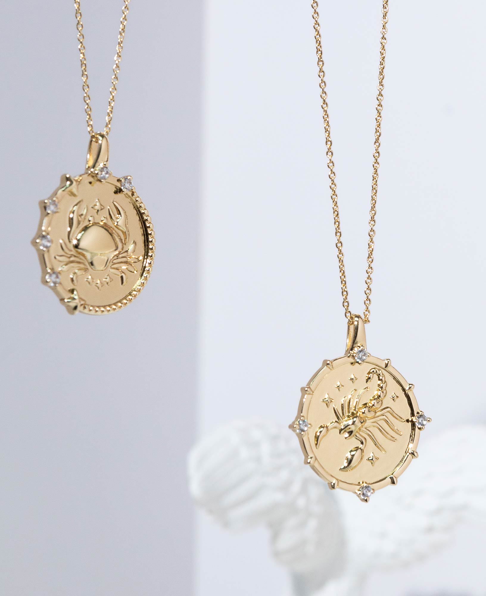 Artistic close-up lifestyle product image of Cancer and Scorpio Horoscope Gold Pendant Necklaces.