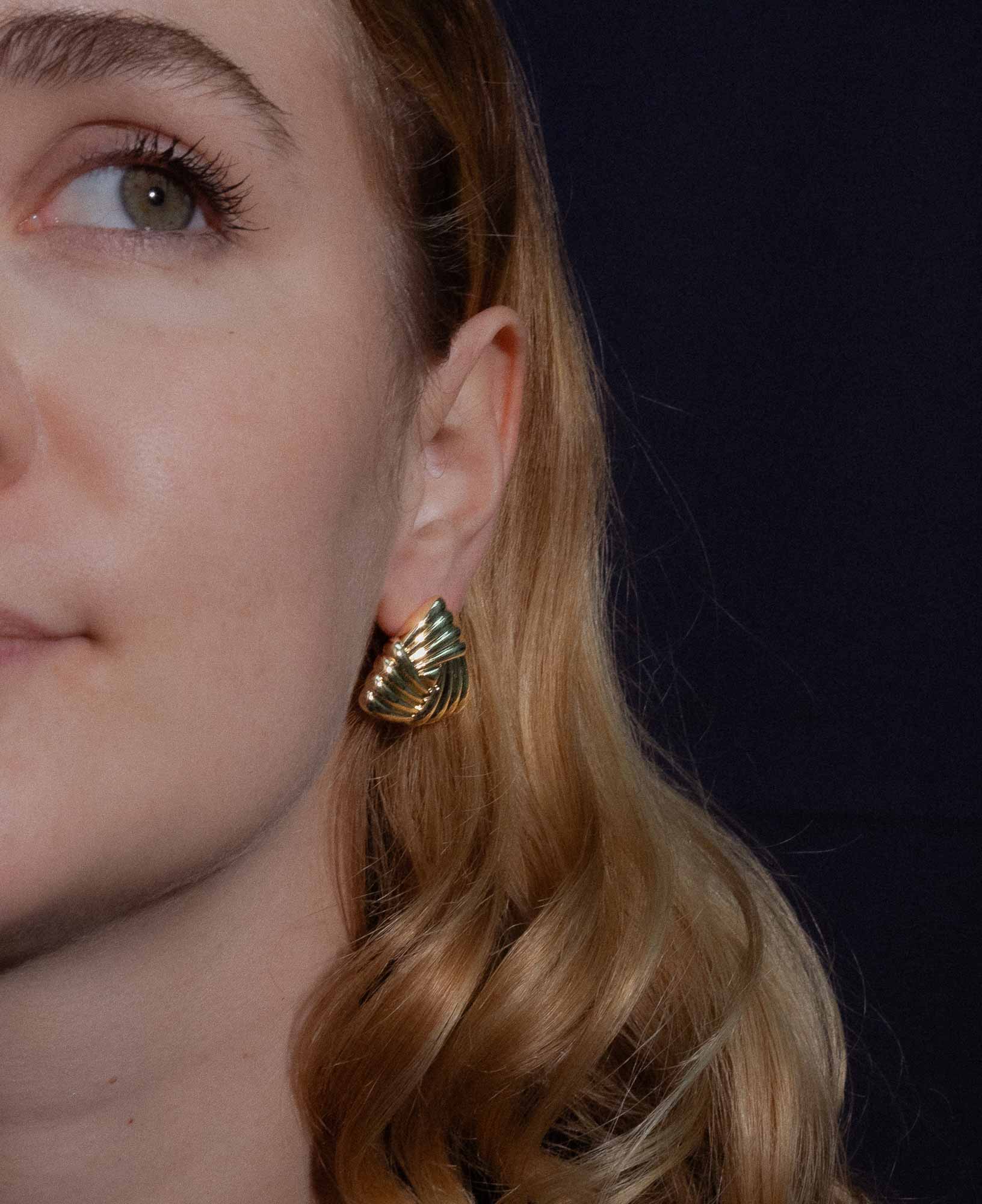 dark and festive close-up shot featuring the Eleanor Triangle Braided Gold Chunky Earrings on a model.