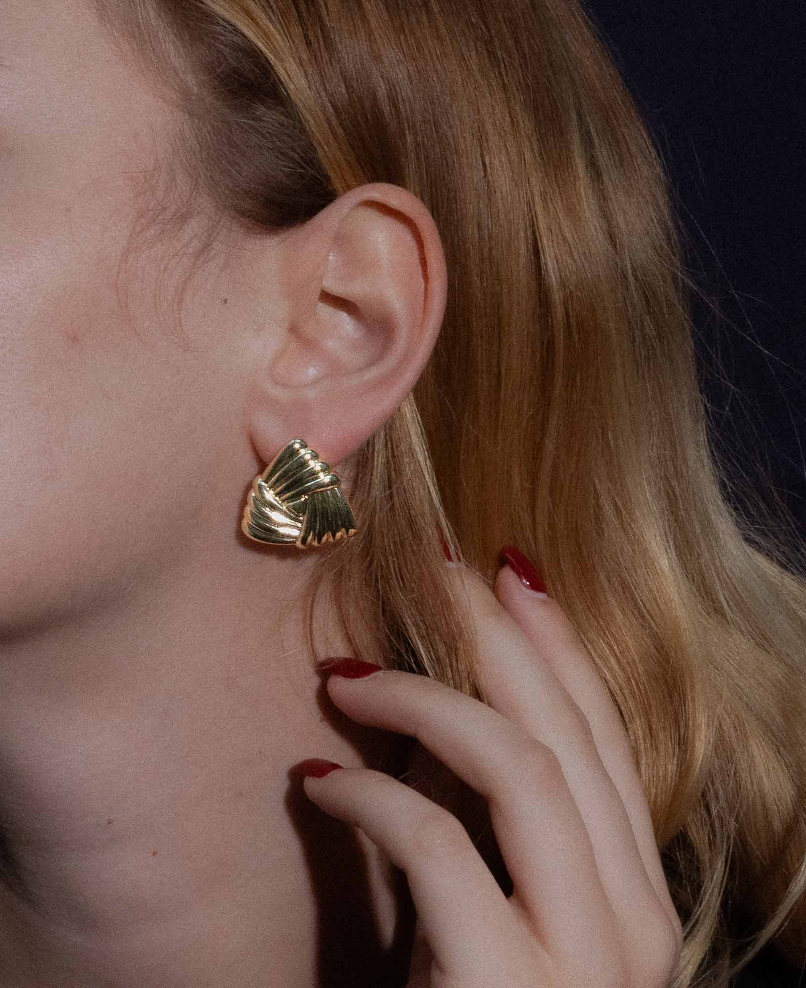 dark and festive close-up shot featuring the Eleanor Triangle Braided Gold Chunky Earrings on a model.