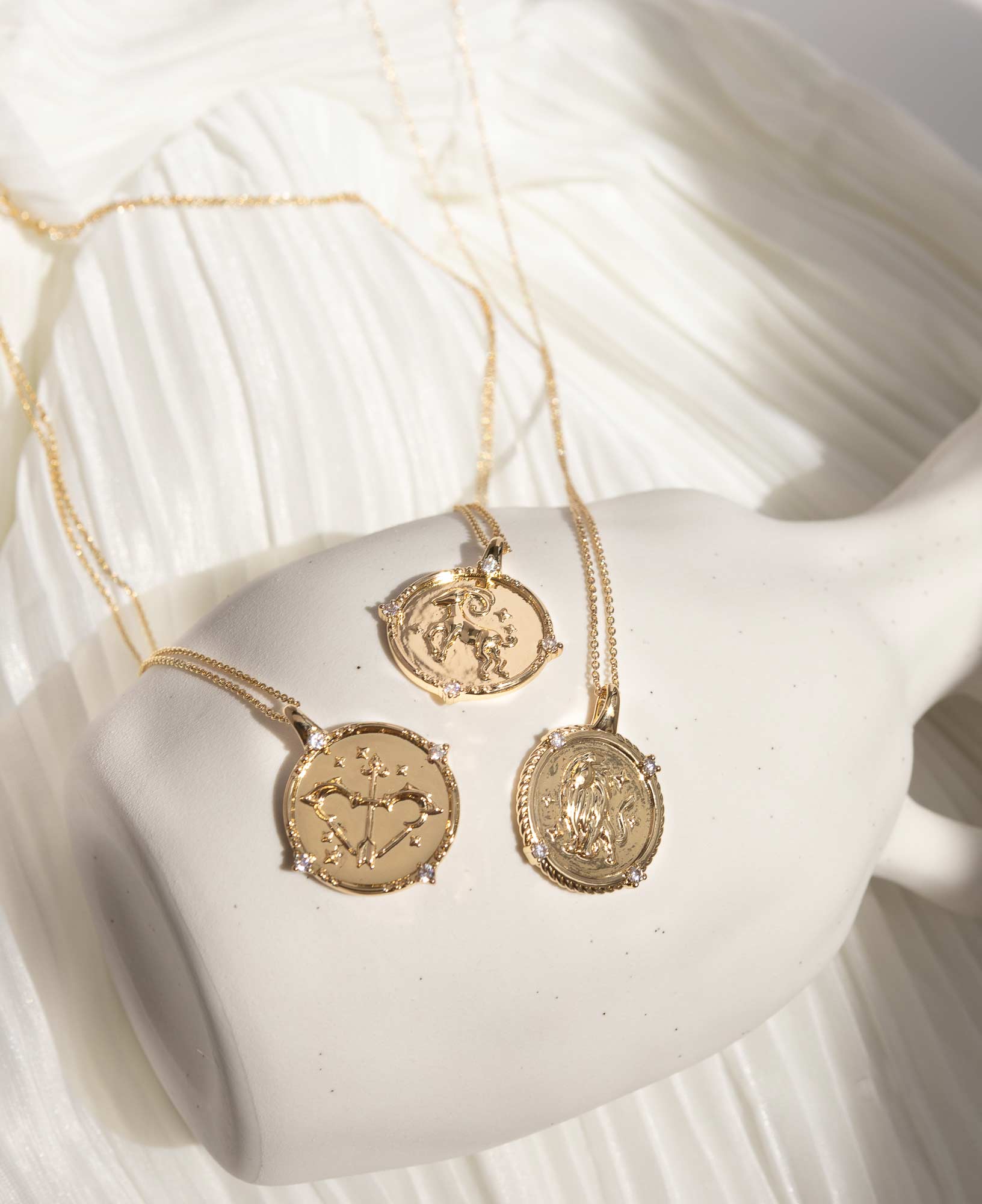 artistic closeup lifestyle picture of the three fire signs' Horoscope Gold Pendant Necklaces placed on a white ceramic vase.