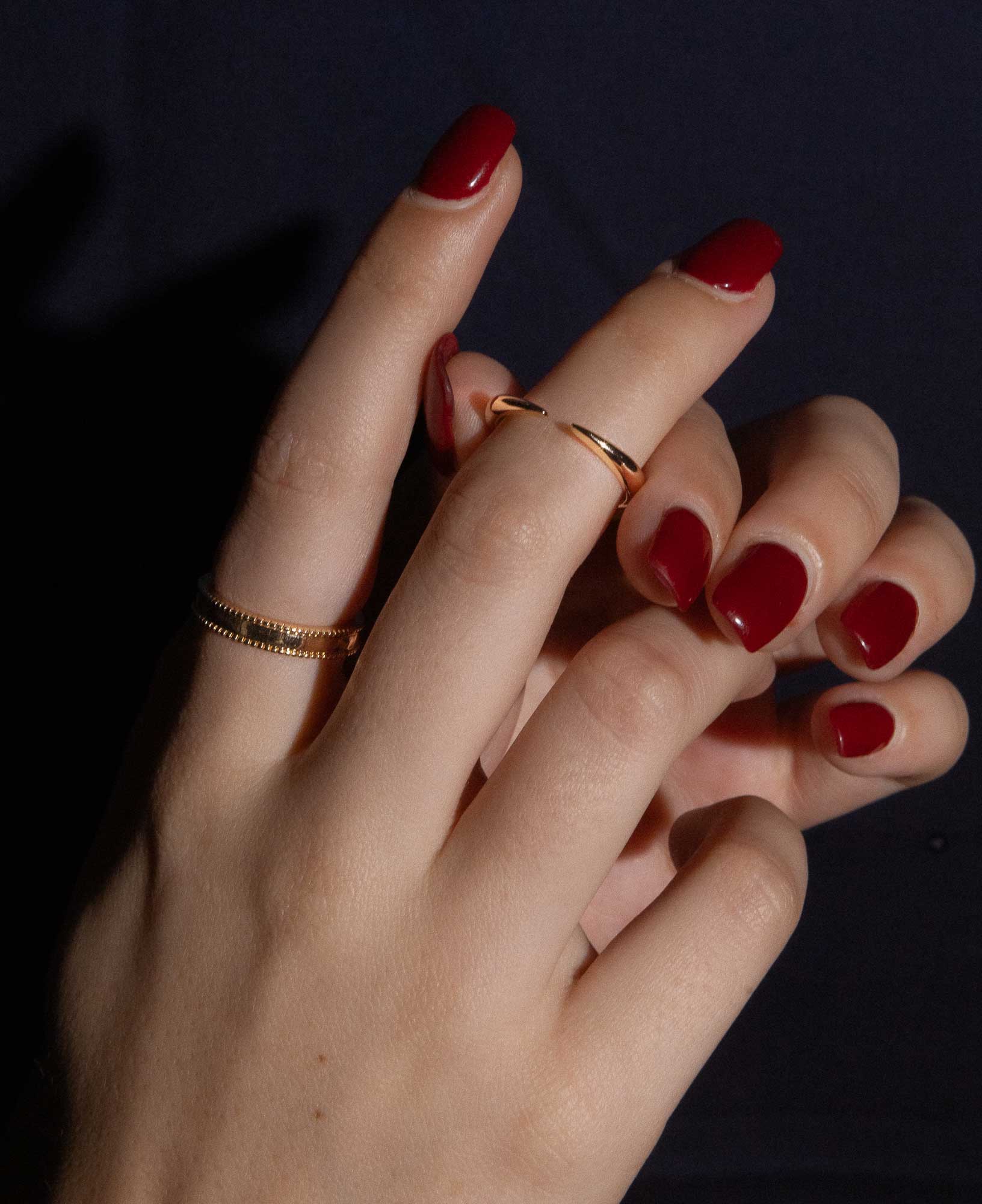 dark and festive close-up shot of model's hand featuring the Gladys Beaded Gold Band Ring and Imogen Gold Cuff Open Ring.