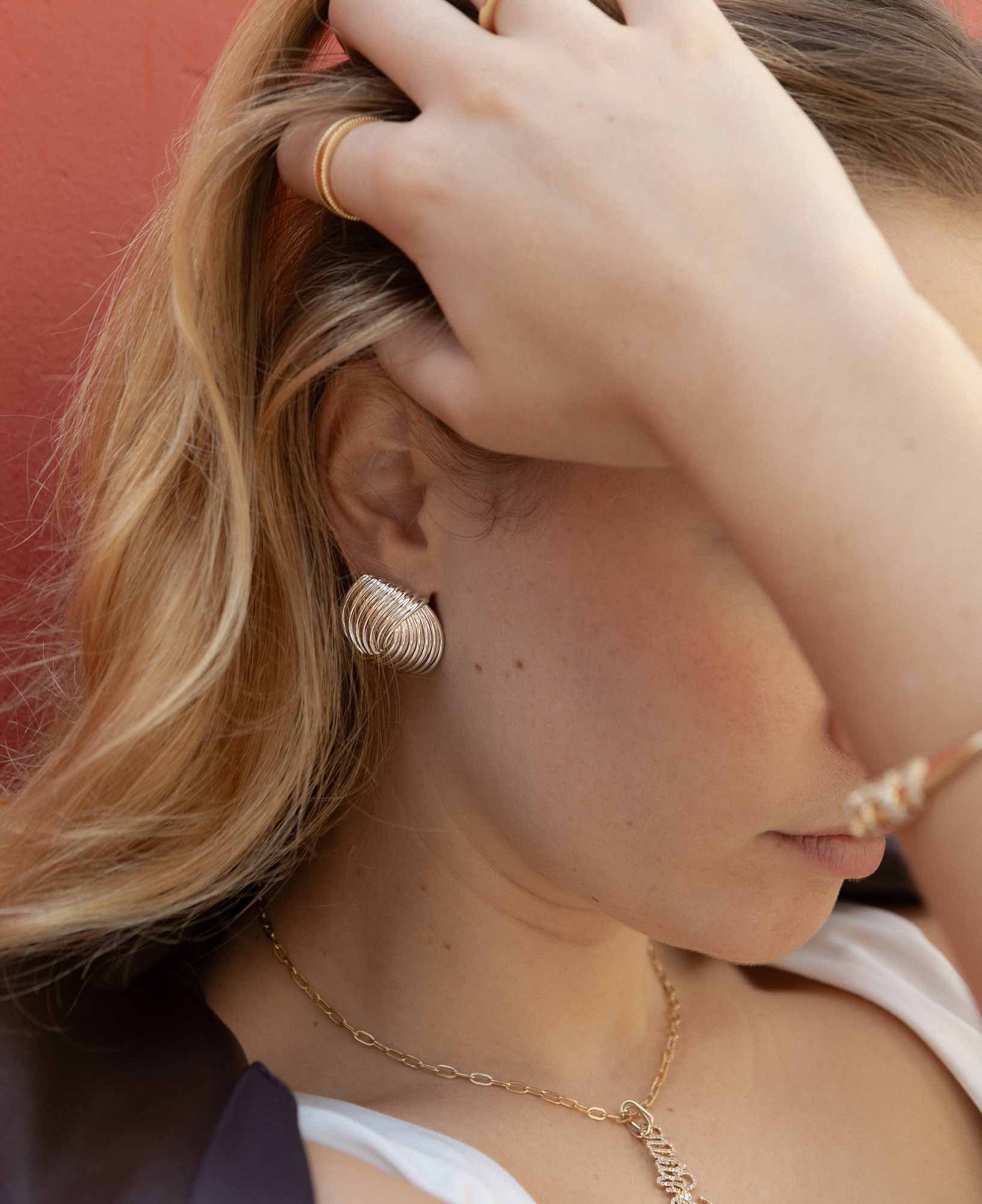  close-up shot of model's hand featuring the Laverne Illusion Knot Silver Statement Earrings.