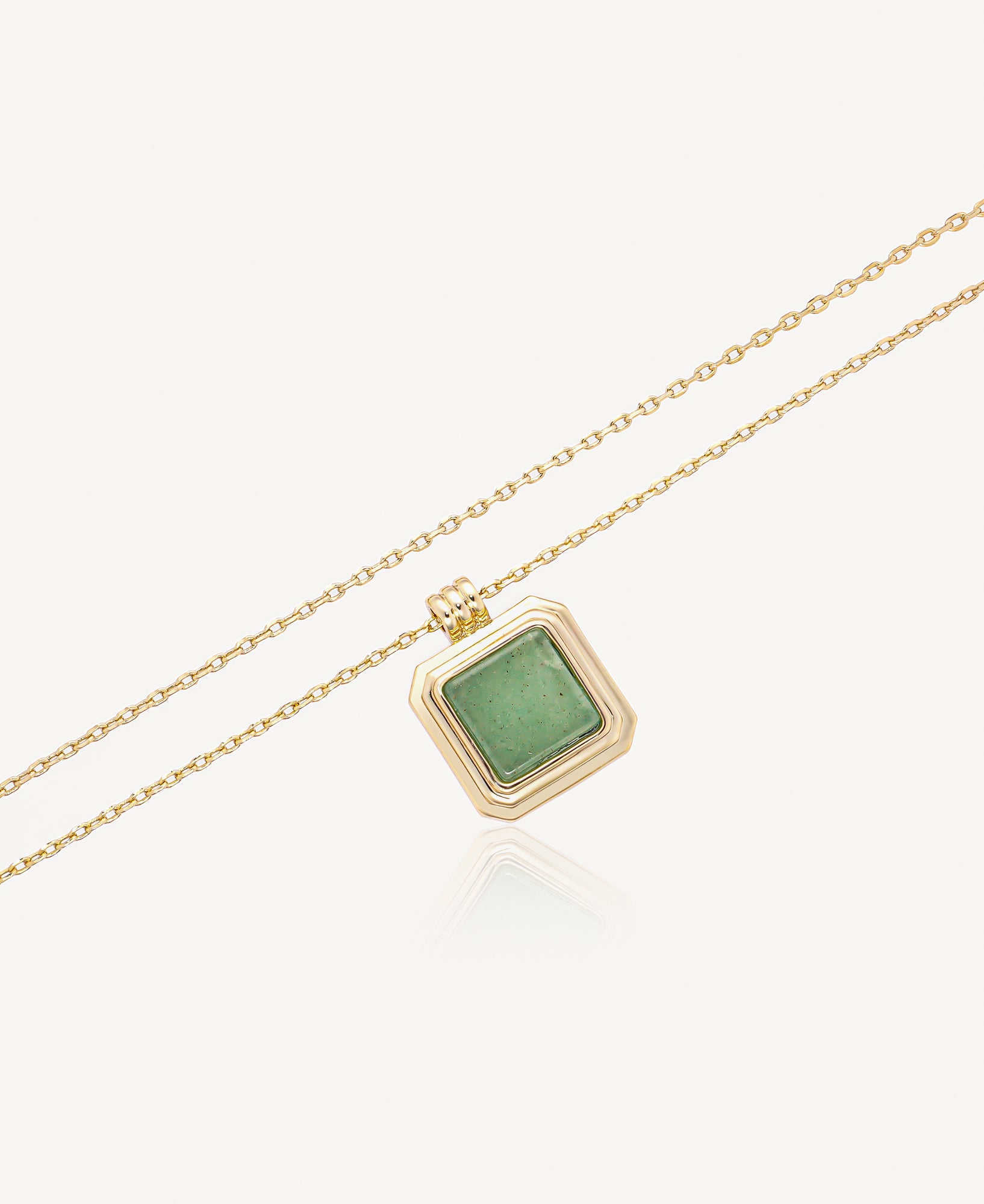 Gold necklace with a green gemstone pendant on a white background