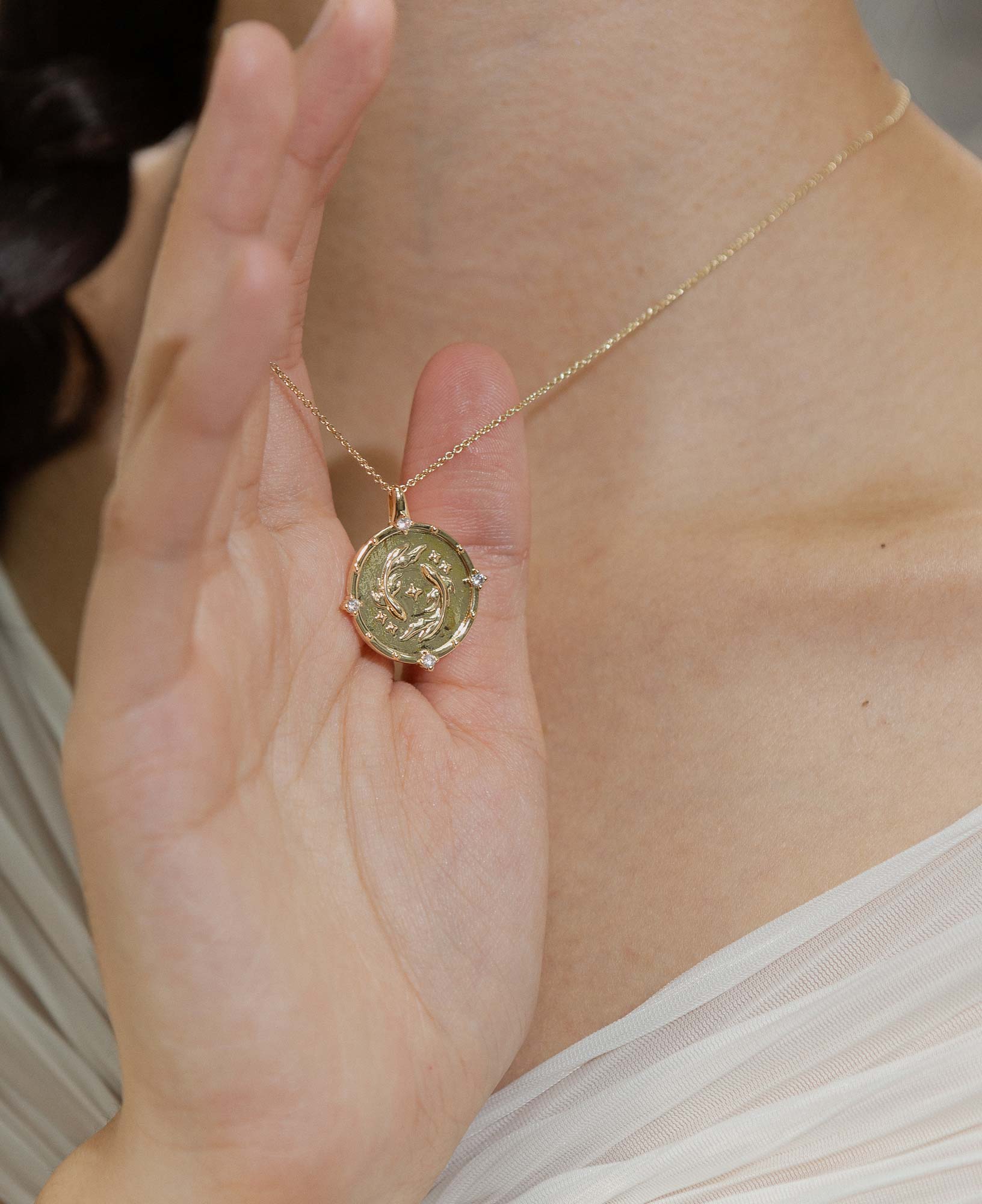 a model wearing the pisces horoscope gold pendant necklace, styled with a white chiffon top.