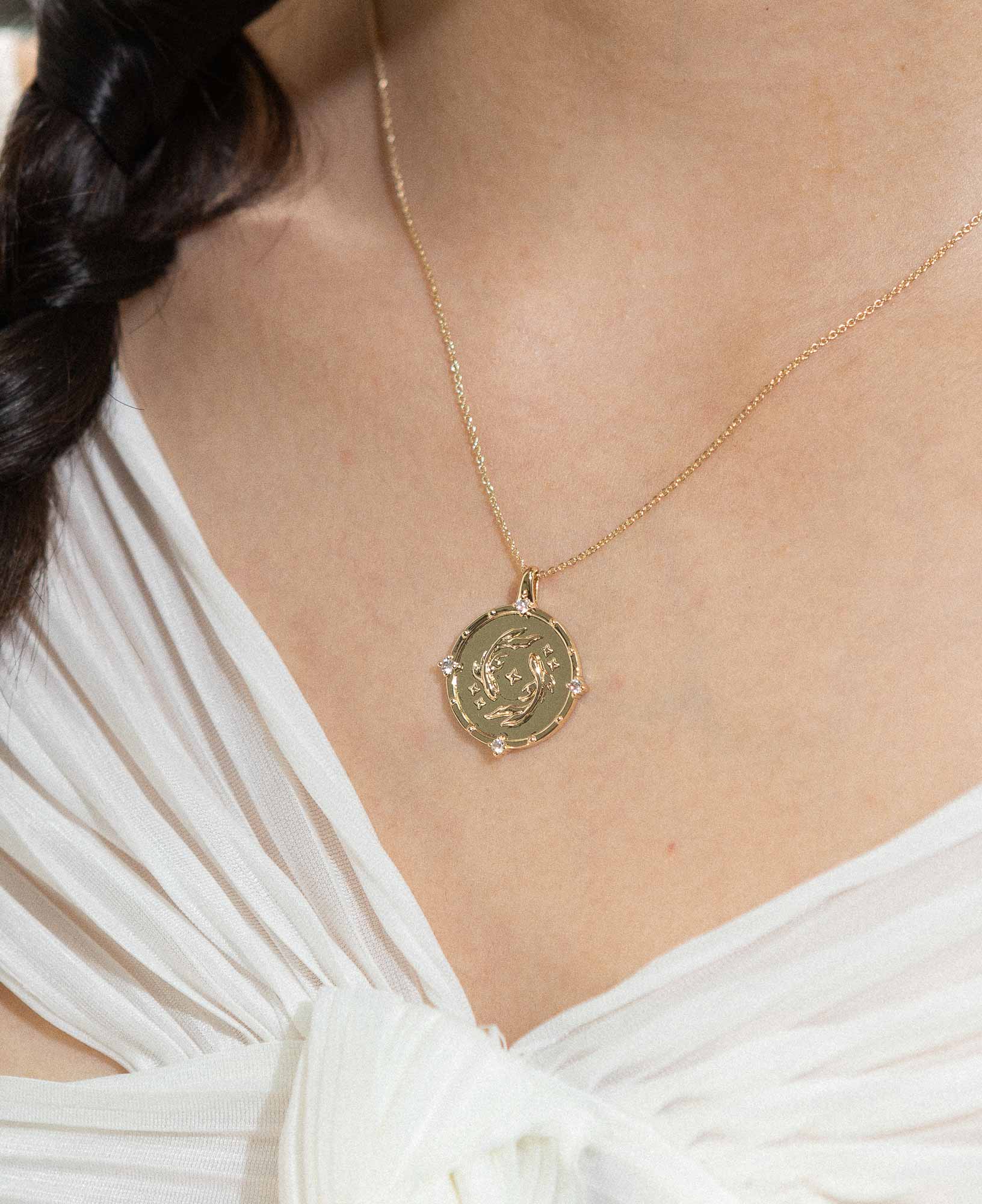 a model wearing the pisces horoscope gold pendant necklace, styled with a white chiffon top.