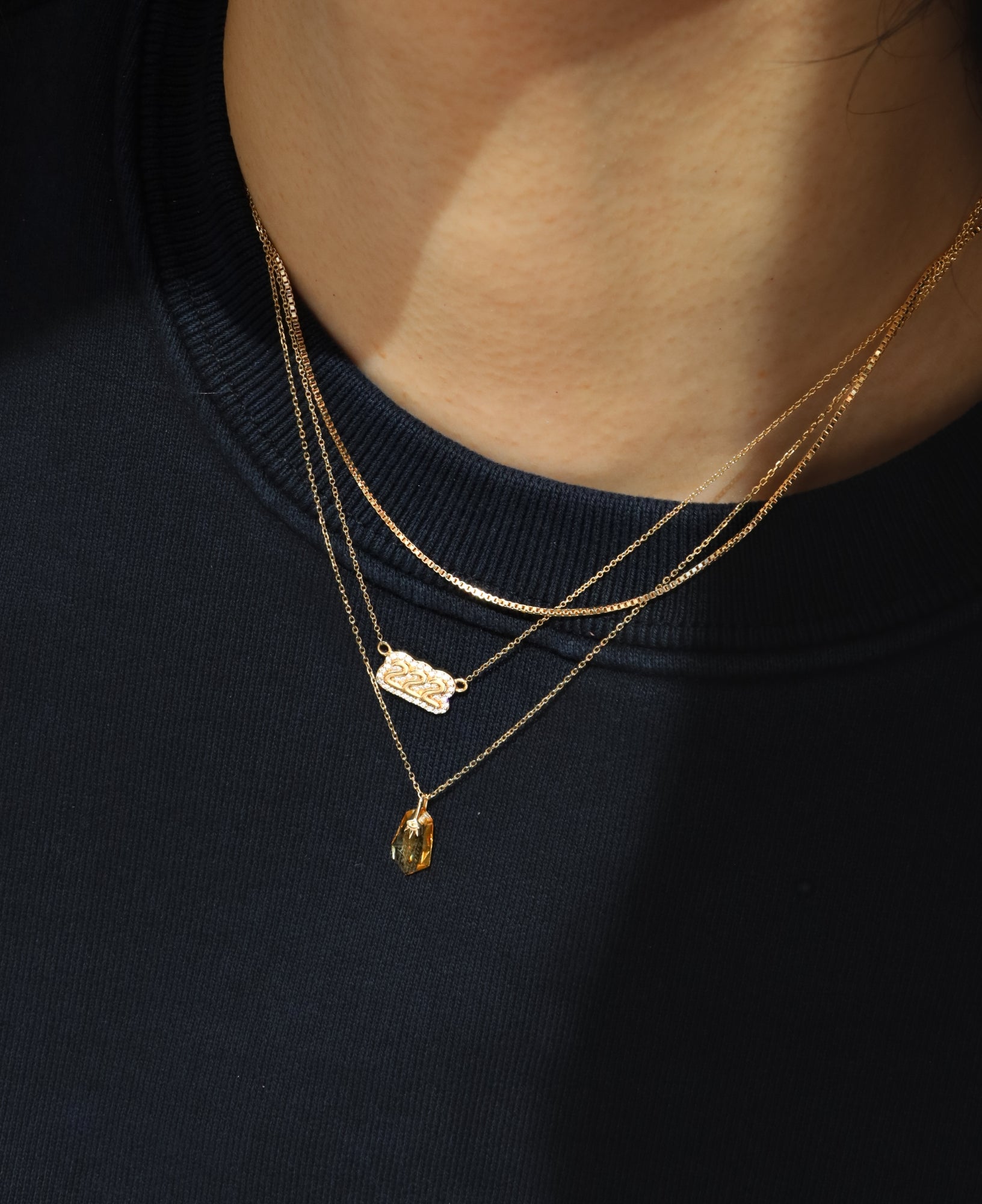 Close-up of a person wearing polly custom diamond bubble number necklace and zephyr 14k Solid Gold citrine pendant necklace on a dark background